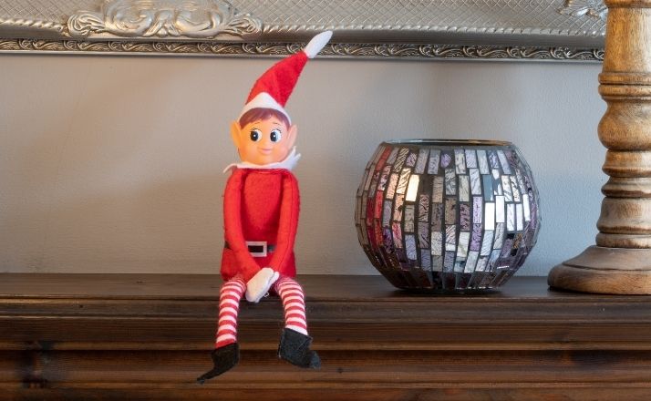 Elf on the Shelf sitting on a shelf with a candle