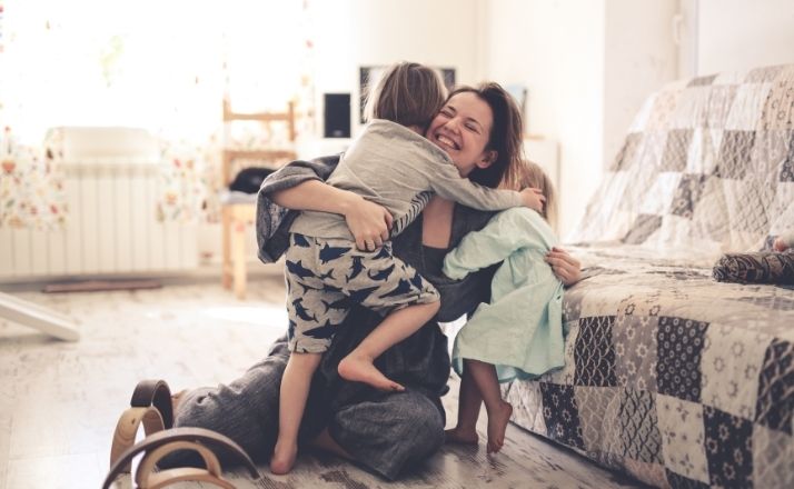 Mom being hugged by two children as she smiles with confidence in the kind of mom she is