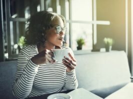 Woman holding a coffee cup looking contently to the side happy without a friend squad
