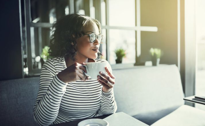 Woman holding a coffee cup looking contently to the side happy without a friend squad