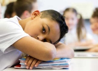 young boy laying his head on desk at school