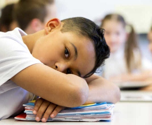 young boy laying his head on desk at school