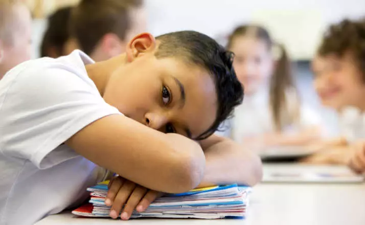 young boy laying his head on desk at school