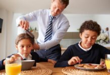 back to school morning of dad brushing daughter's hair while daughter and son eat breakfast