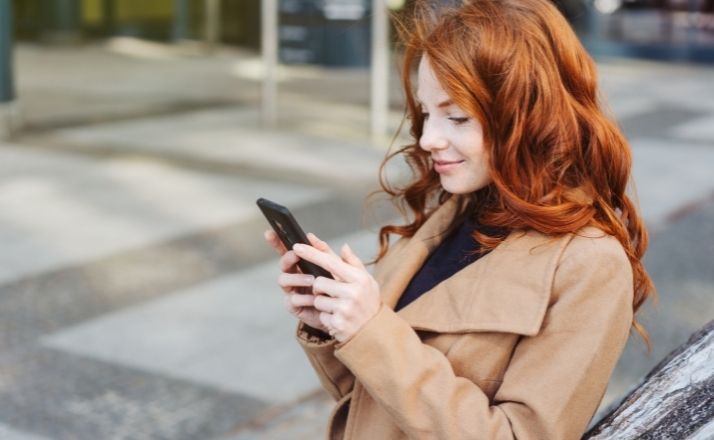 Woman smiling and creating better tweets on Twitter on her cellphone