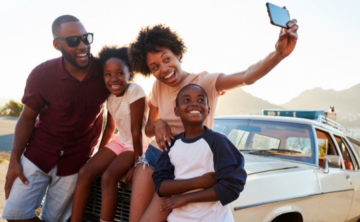 family selfie outside car on their family road trip