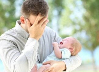 First-time parent dad covers face while holding screaming infant