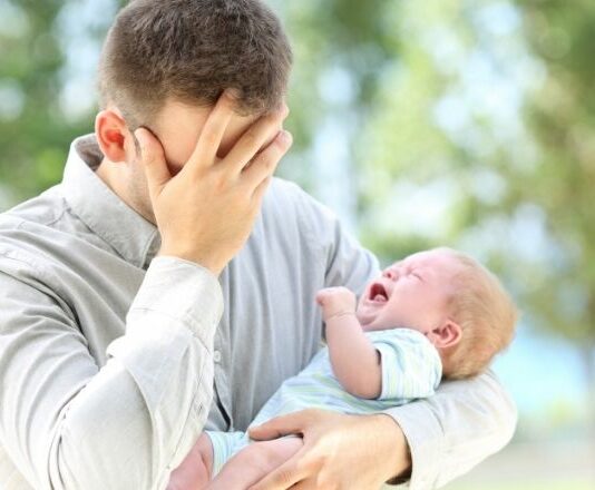 First-time parent dad covers face while holding screaming infant
