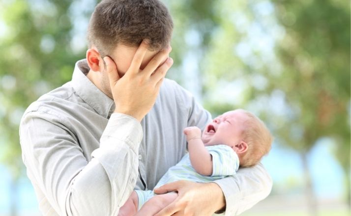 First-time parent dad covers face while holding screaming infant