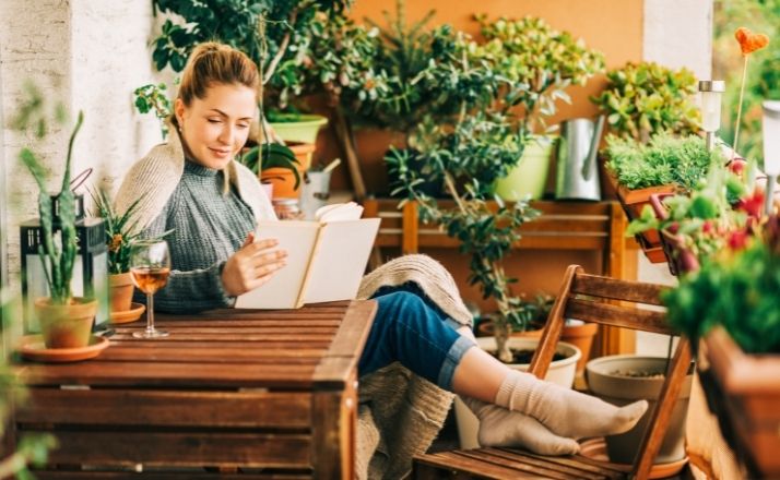 woman reading a book while sitting on a porch surrounded by plants on a mommy vacation