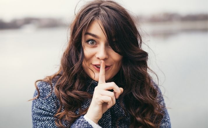 Woman with finger to lips holding in secrets