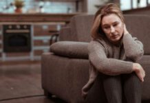 Woman wearing brown squared trousers feeling depressed sitting on the floor next to her couch. This is depression