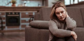 Woman wearing brown squared trousers feeling depressed sitting on the floor next to her couch. This is depression