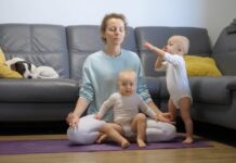 Mom in yoga pants closing her eyes as twin babies crawl around her