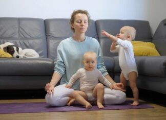 Mom in yoga pants closing her eyes as twin babies crawl around her