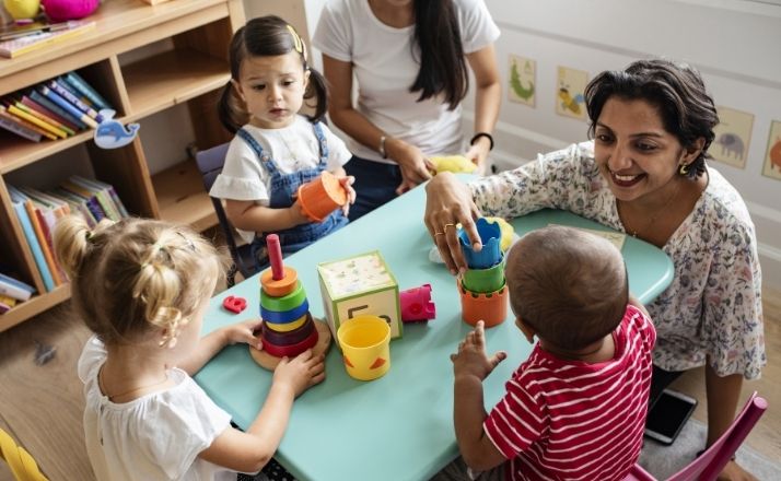 day care center two women playing with three toddlers at table