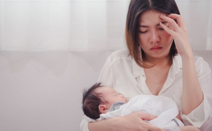 intrusive thoughts woman holding baby with hand on head