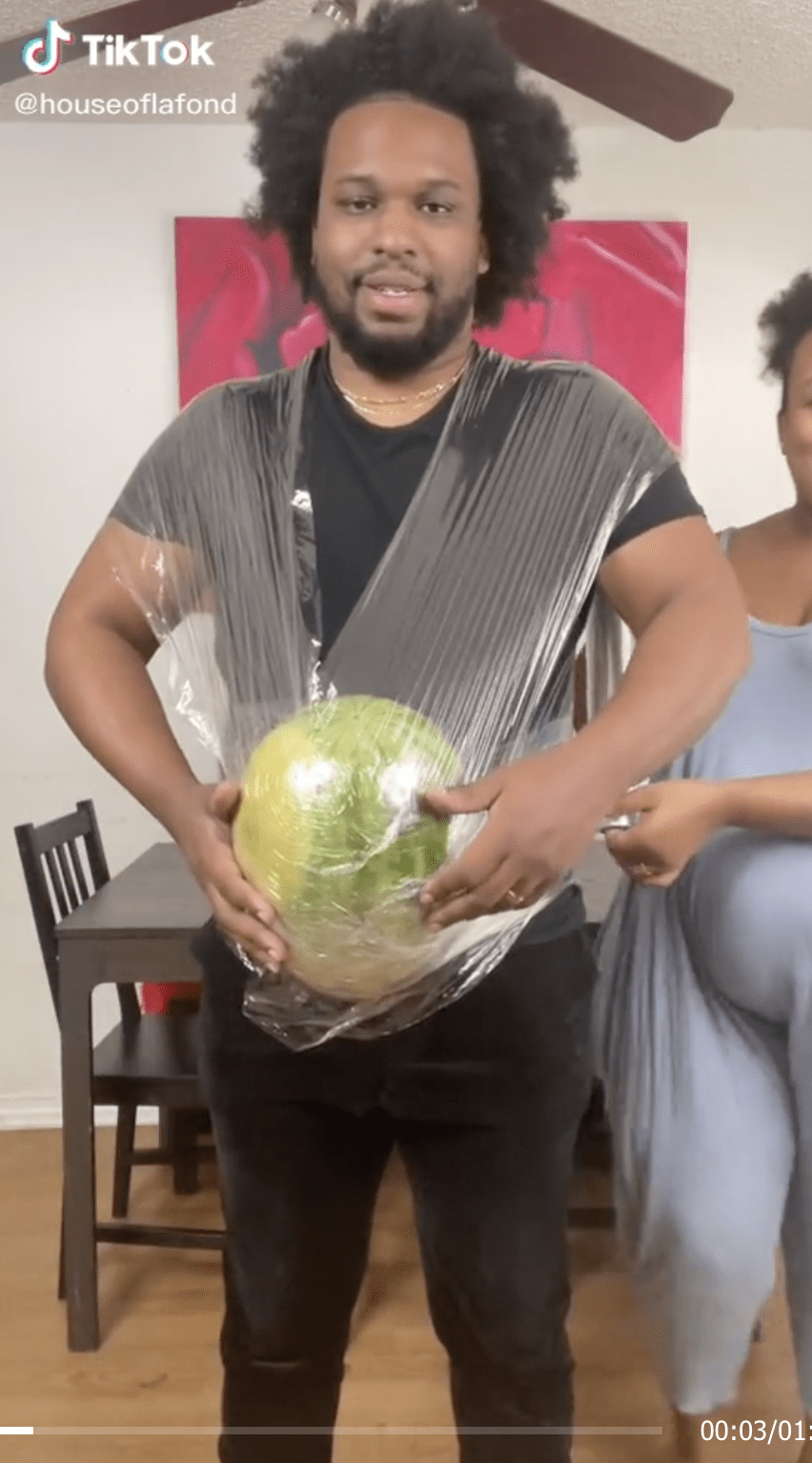 Wife strapping watermelon to husband's belly