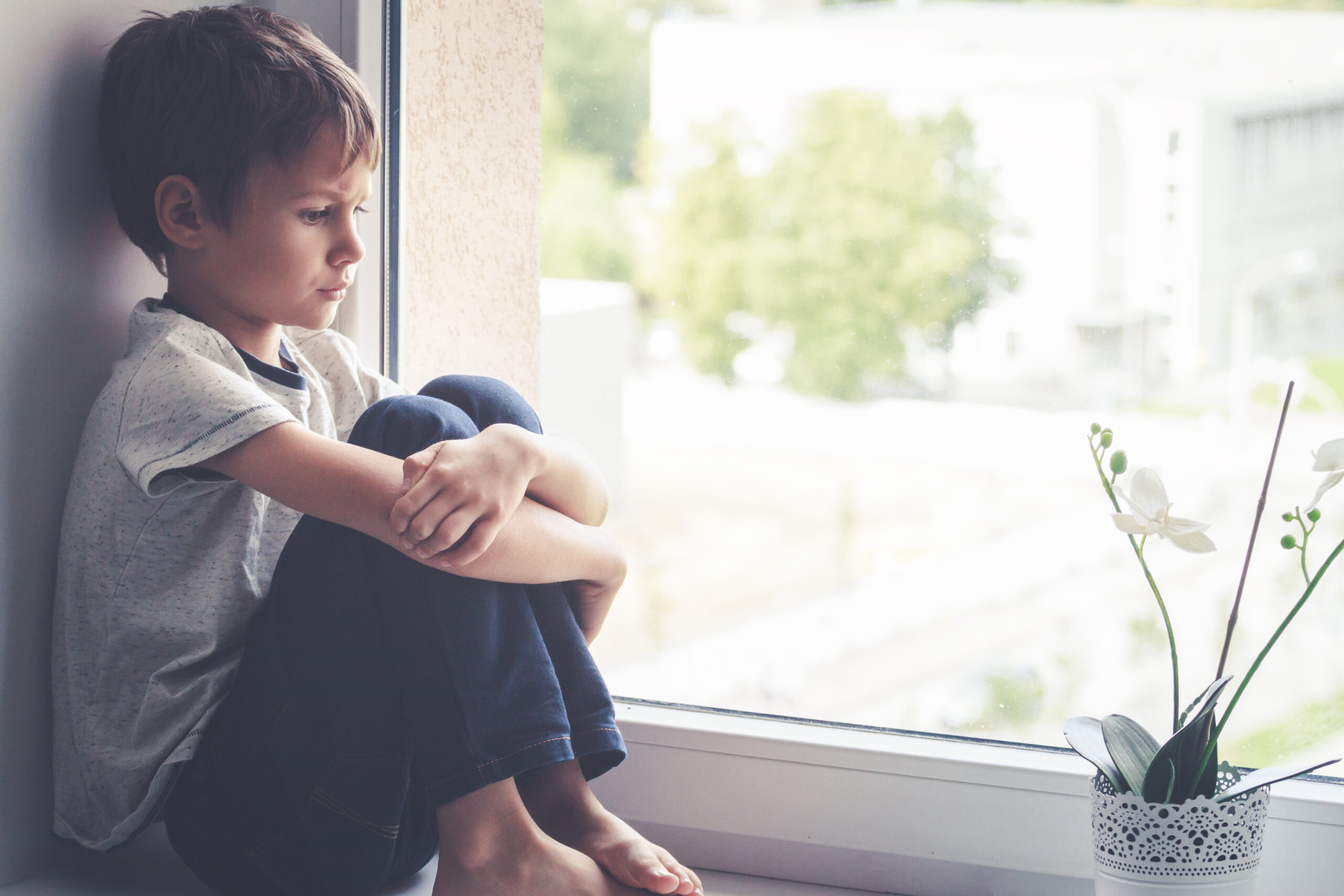 Sad child sitting on window sill