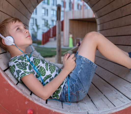 smiling boy with smartphone and headphones listening to music or playing game