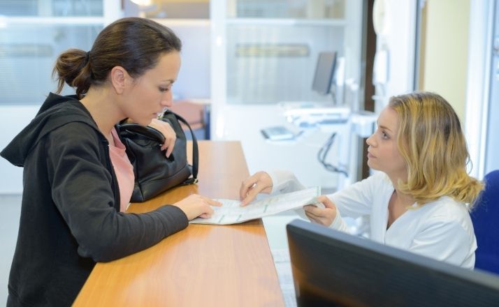 Mom at medical office counter explaining situation of divorced parents to clerk