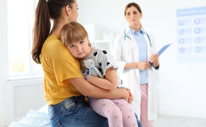 Mom holding sad child in pediatrician office