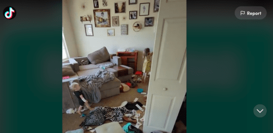 Screenshot of TikTok video by @themessymama4 showing her living room covered in clothing and toys, two children are in the background