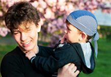 Two brothers - a young boy and a teen together fooling around during a photo shoot against the background of sakura blossoms with pink flowers. The brothers are friends and look after each other