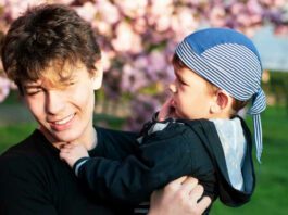 Two brothers - a young boy and a teen together fooling around during a photo shoot against the background of sakura blossoms with pink flowers. The brothers are friends and look after each other