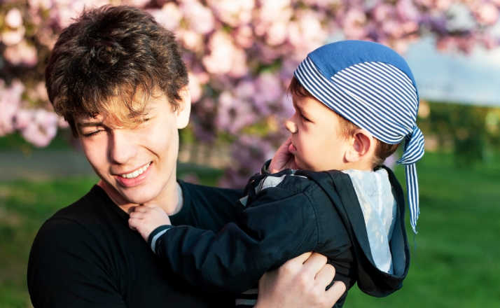 Two brothers - a young boy and a teen together fooling around during a photo shoot against the background of sakura blossoms with pink flowers. The brothers are friends and look after each other