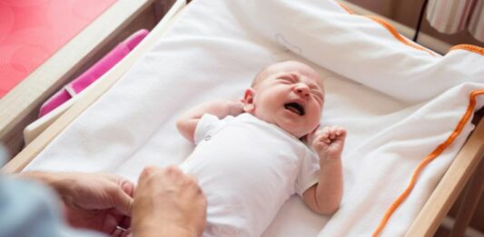 baby crying on a changing table with mom nearby as an example of baby safety tips