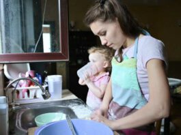 A young woman is busy cooking, while her little daughter is playing nearby. Mom and baby doing household chores