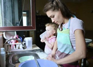 A young woman is busy cooking, while her little daughter is playing nearby. Mom and baby doing household chores