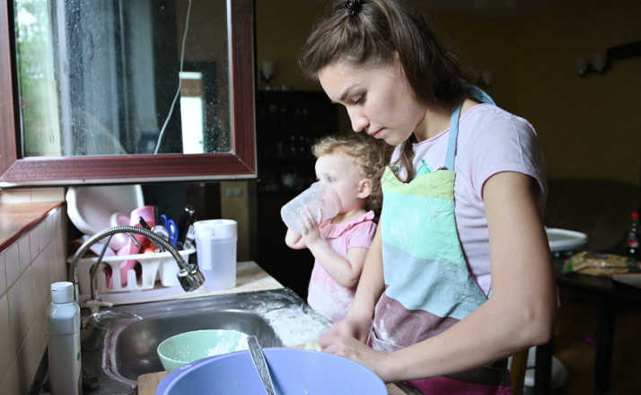 A young woman is busy cooking, while her little daughter is playing nearby. Mom and baby doing household chores