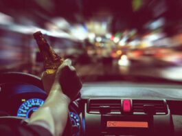 Man drink beer while driving at night in the city dangerously, left hand drive system