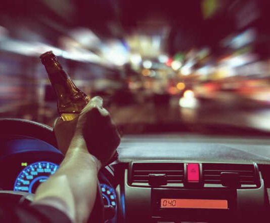 Man drink beer while driving at night in the city dangerously, left hand drive system