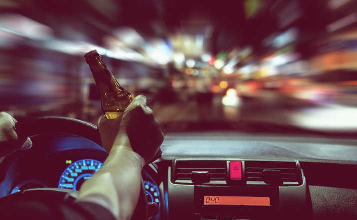 Man drink beer while driving at night in the city dangerously, left hand drive system