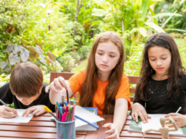Three children sitting at an outside table doing their homeschool assignments