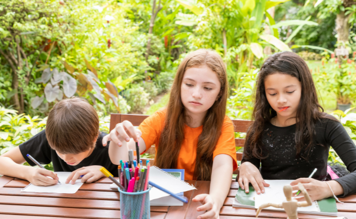 Three children sitting at an outside table doing their homeschool assignments