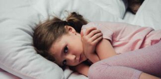 frightened child looking at camera while lying in bed and hugging herself with arms