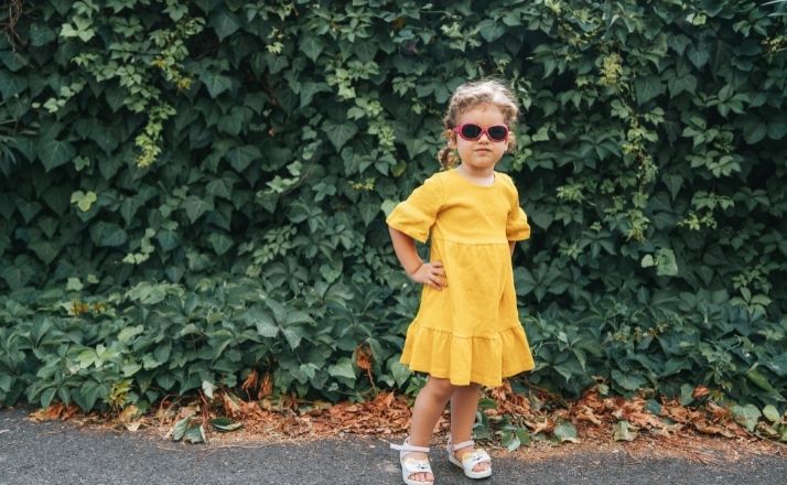 Toddler with yellow dress, sunglasses, and hands on her hips