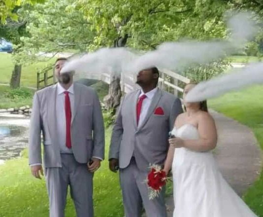Bride and groom and groomsman vaping in wedding photo