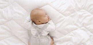 newborn baby in white bodysuit and gray romper sleep sweet on his tummy on white blanket, cute baby sleep top view