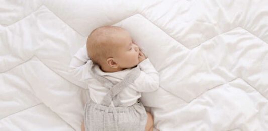 newborn baby in white bodysuit and gray romper sleep sweet on his tummy on white blanket, cute baby sleep top view