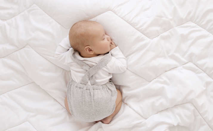 newborn baby in white bodysuit and gray romper sleep sweet on his tummy on white blanket, cute baby sleep top view