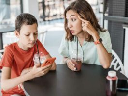 Emotional conflict between mother and son about smartphone addiction in cafe. An angry mom and a teenager ignoring her.