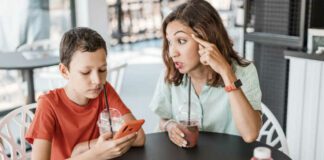 Emotional conflict between mother and son about smartphone addiction in cafe. An angry mom and a teenager ignoring her.