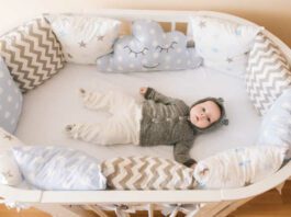 Beautiful newborn baby lying in an oval bed with beautiful bumpers in delicate gray, blue, white tones