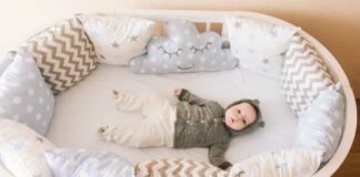 Beautiful newborn baby lying in an oval bed with beautiful bumpers in delicate gray, blue, white tones