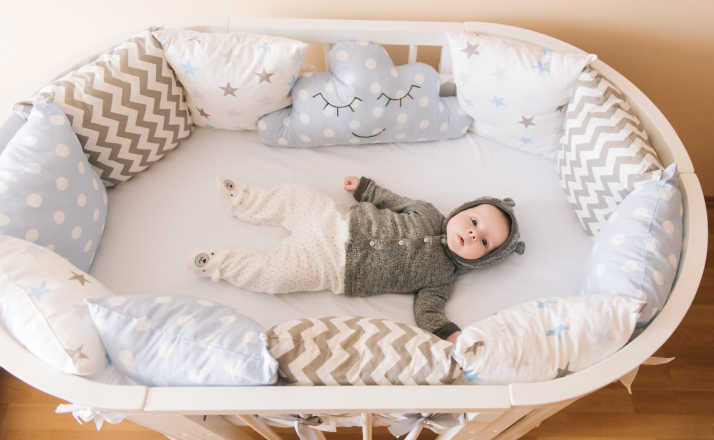 Beautiful newborn baby lying in an oval bed with beautiful bumpers in delicate gray, blue, white tones